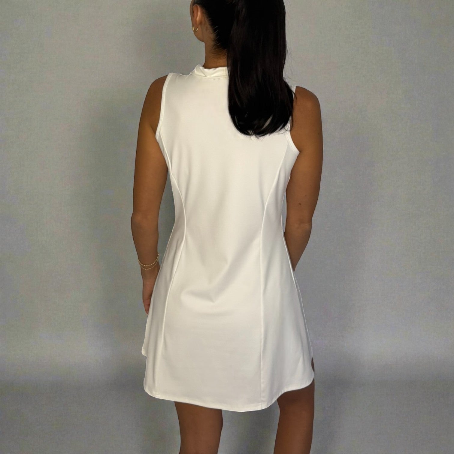 Woman wearing a white sleeveless dress against a plain background