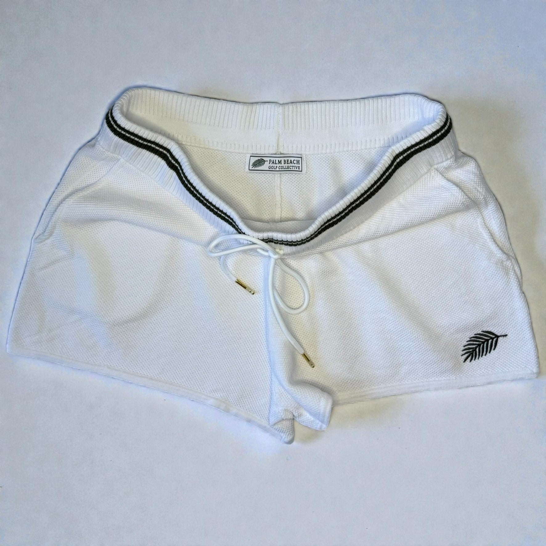 White shorts with dark green trim and logos on a light gray background