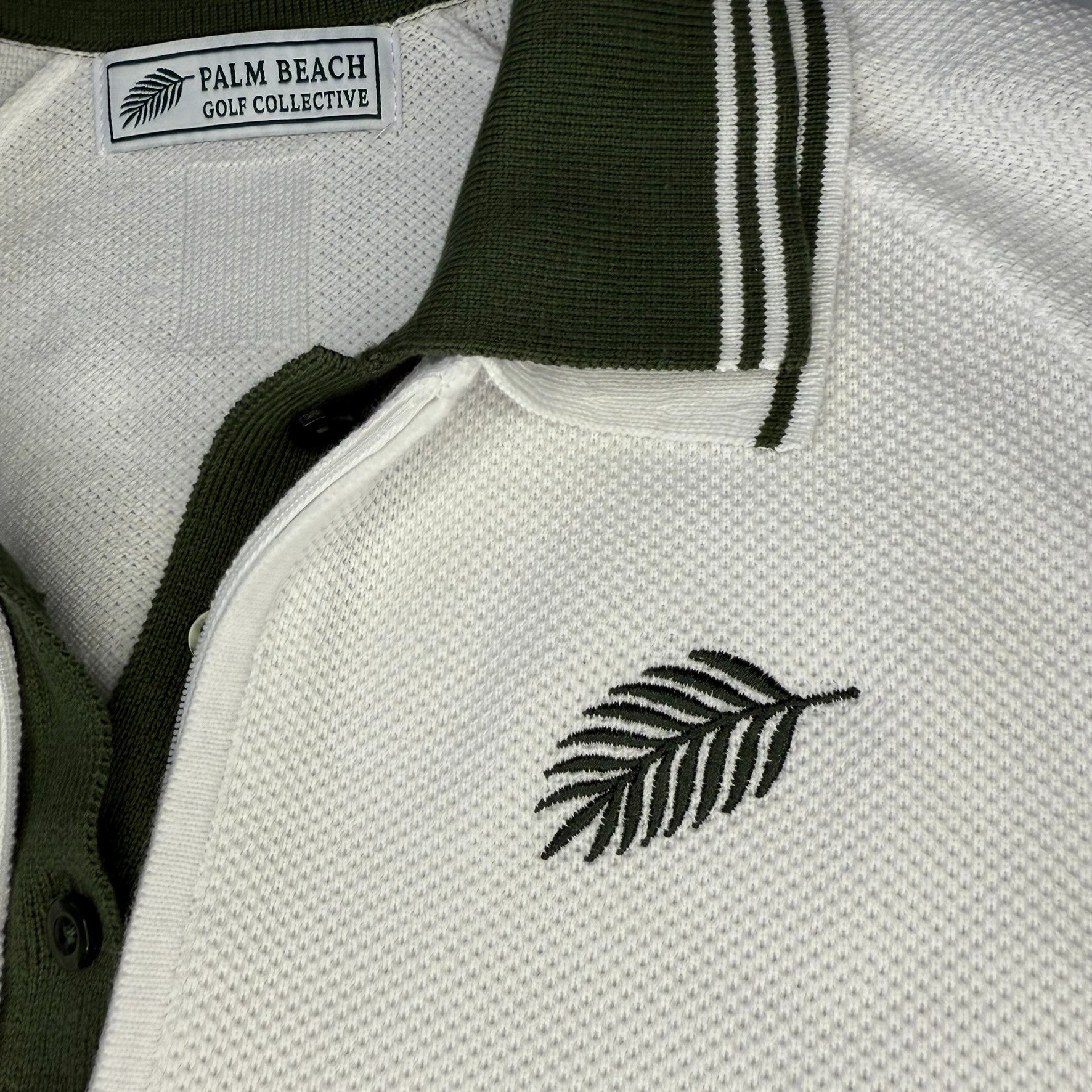 Close-up of a white polo shirt with green palm leaf embroidery and 'Palm Beach Golf Collective' label.