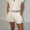 Person wearing a white polo shirt and shorts set with a logo on a plain background