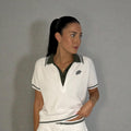 Woman wearing a white polo shirt with green accents against a gray background