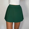 Green pleated skirt worn over a white top on a plain background