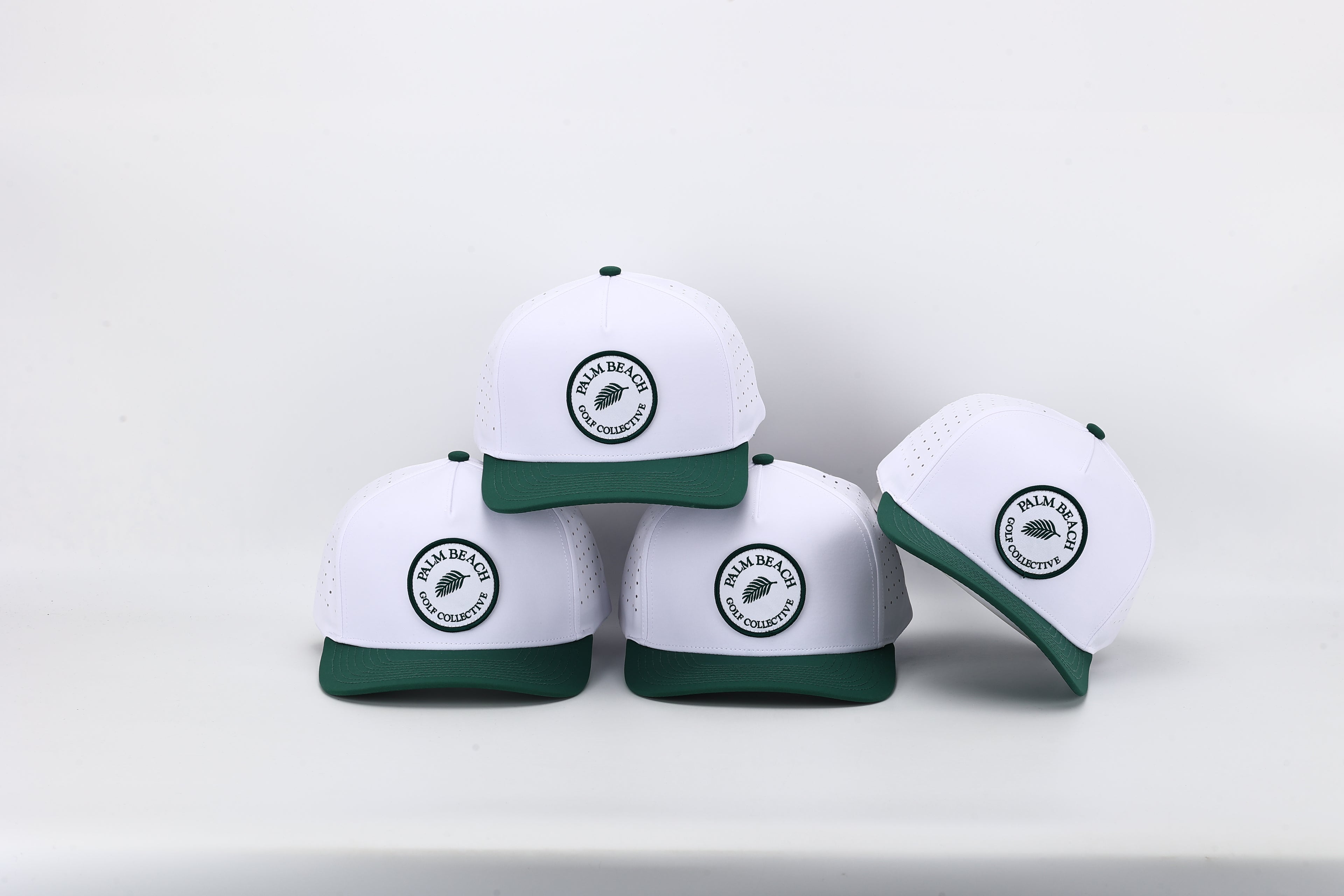 Four white baseball caps with green accents and logos on a light gray background
