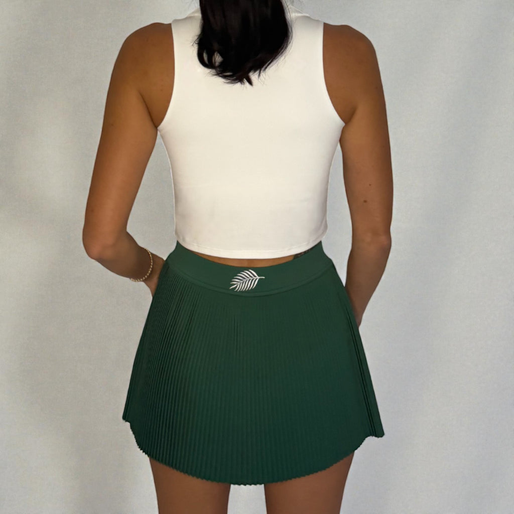 Person wearing a white sleeveless top and green pleated skirt on a plain background