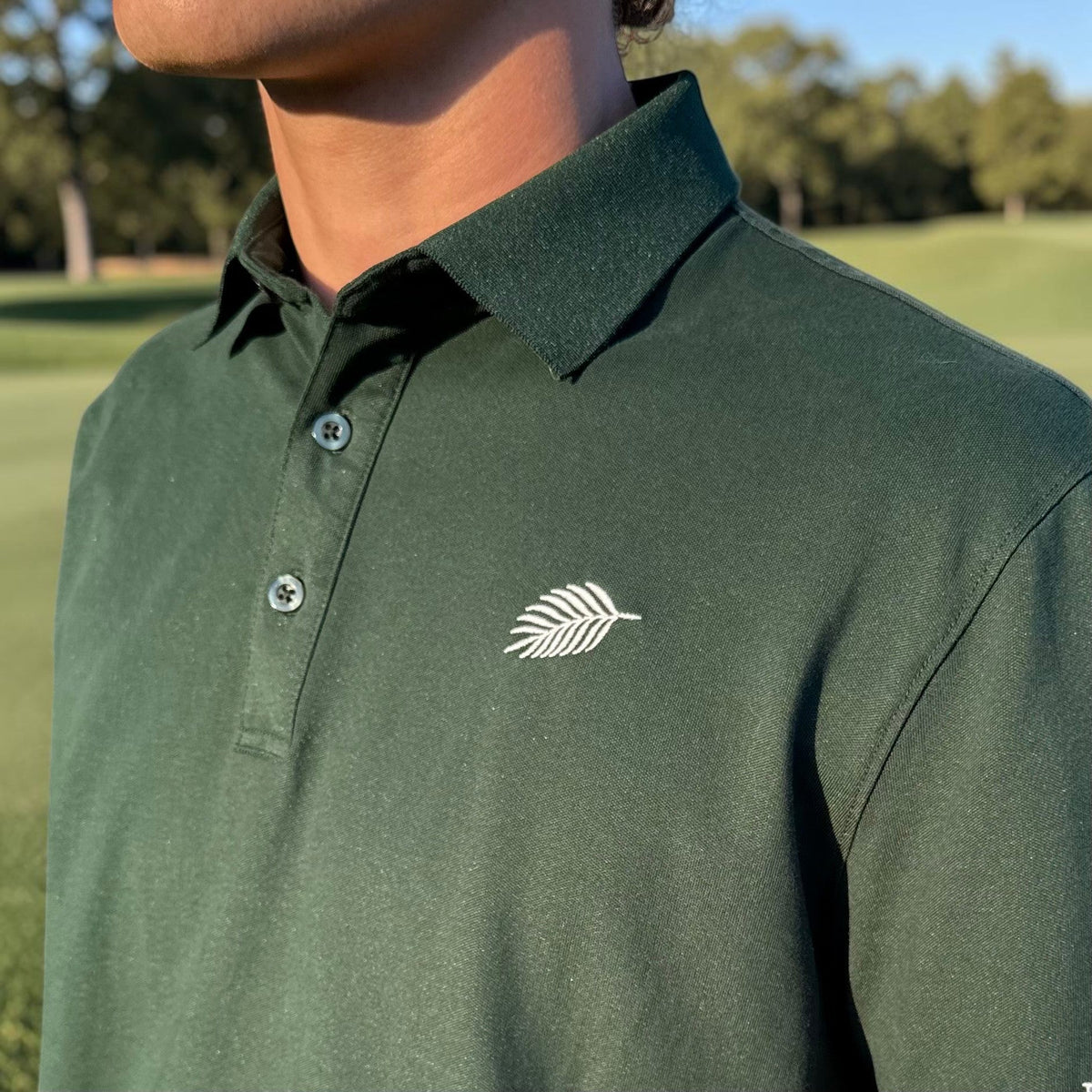 PBGC forest green performance golf polo with a three-button placket and white palm leaf logo on the chest