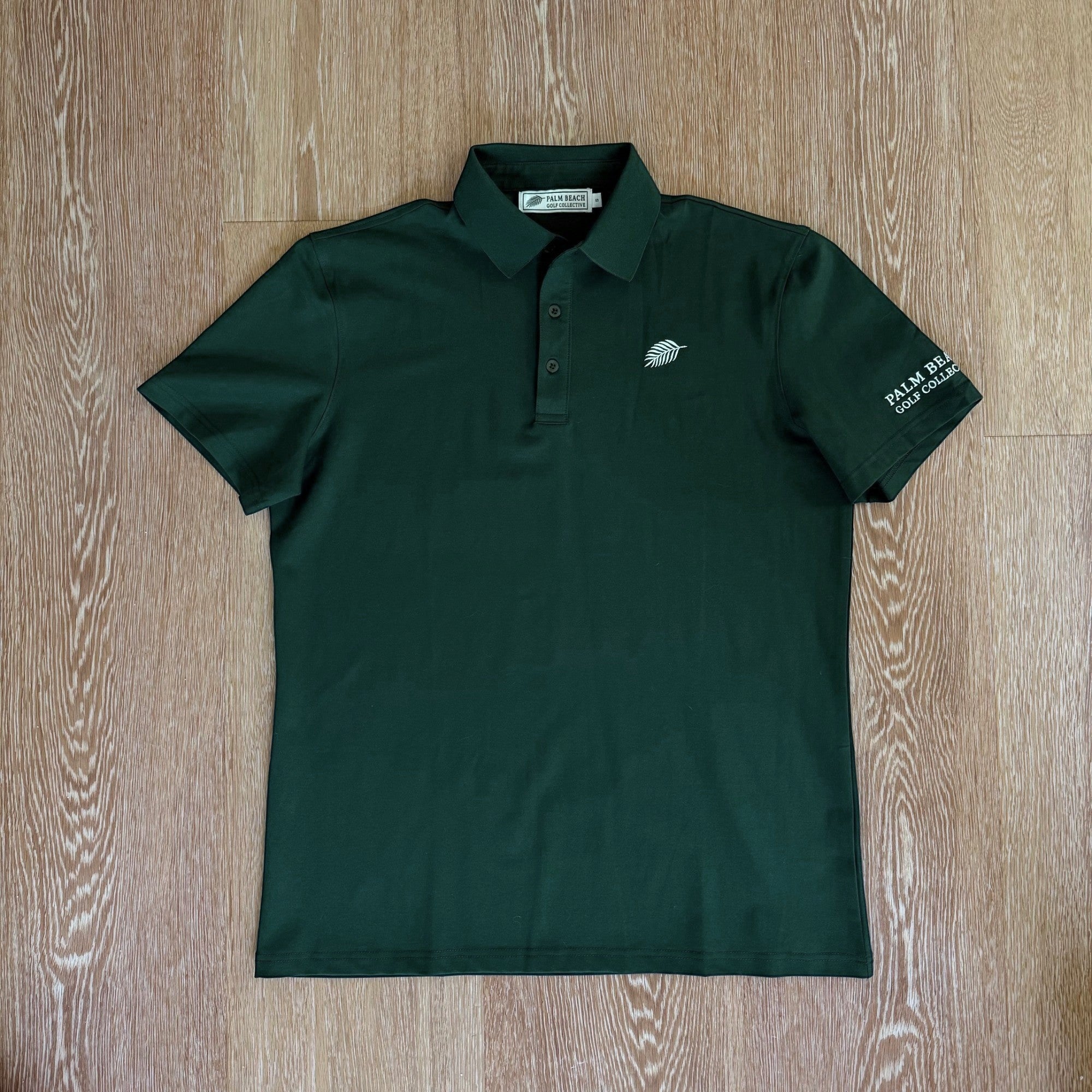 PBGC deep forest green performance golf polo with a three-button placket, structured collar, and palm leaf logo.
