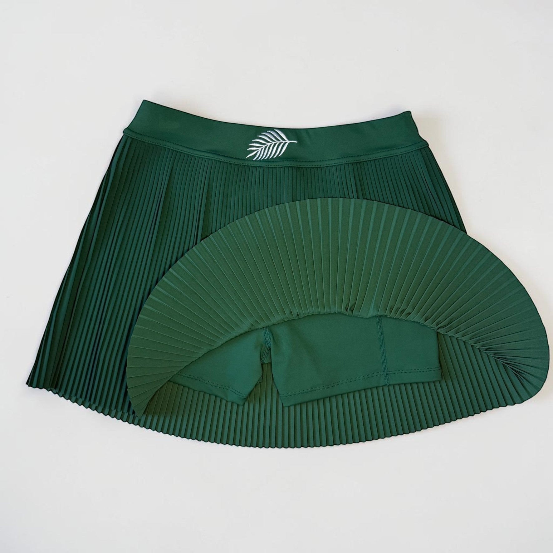 PBGC forest green pleated athletic skirt with built-in shorts and a white palm leaf logo on the high-rise waistband.