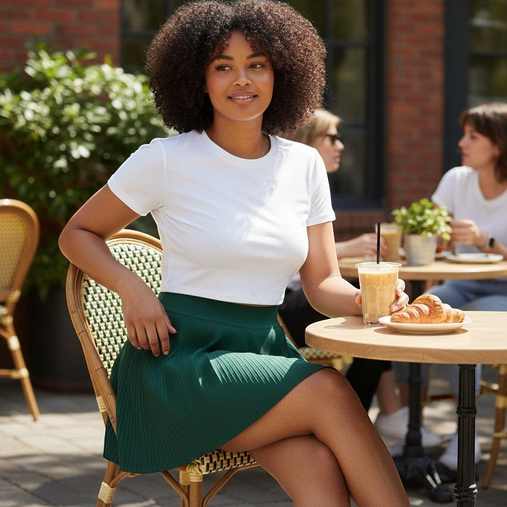 PBGC On the Green Skirt in dark green with pleated detailing, worn by a model at an outdoor cafe table.