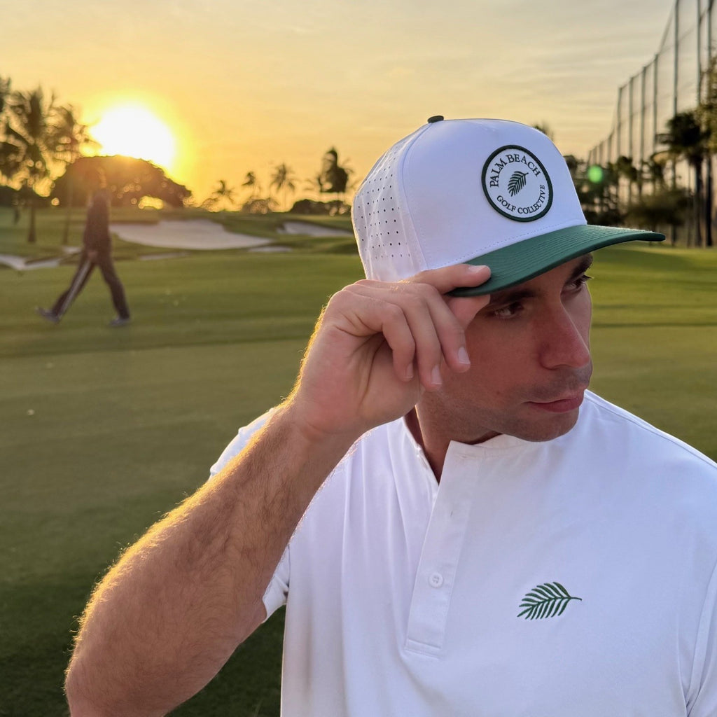 PBGC Palm Patch Hat with white perforated crown and green bill worn by a man on a golf course at sunset