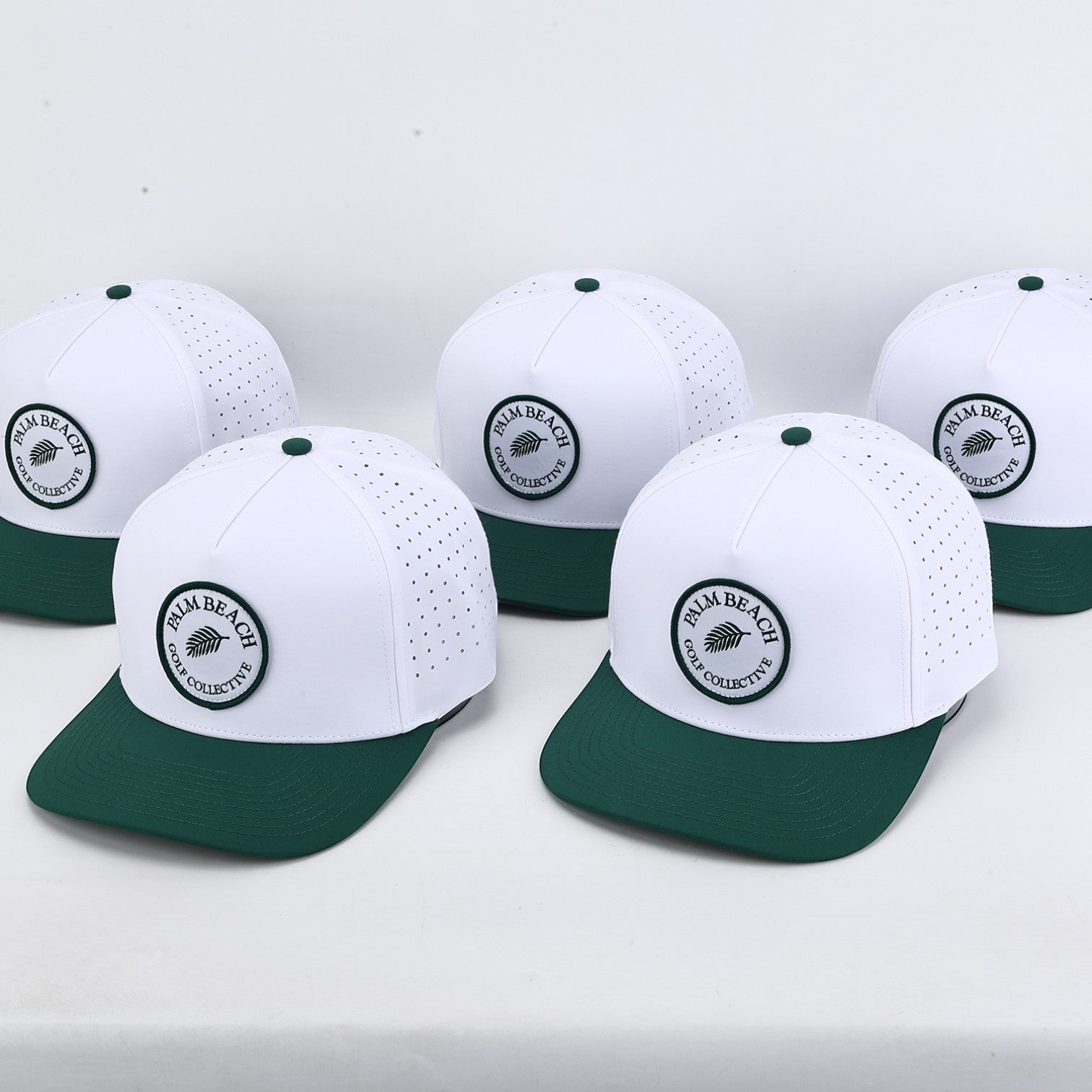 Five PBGC Palm Patch hats with white perforated crowns and deep green bills arranged on a white surface.