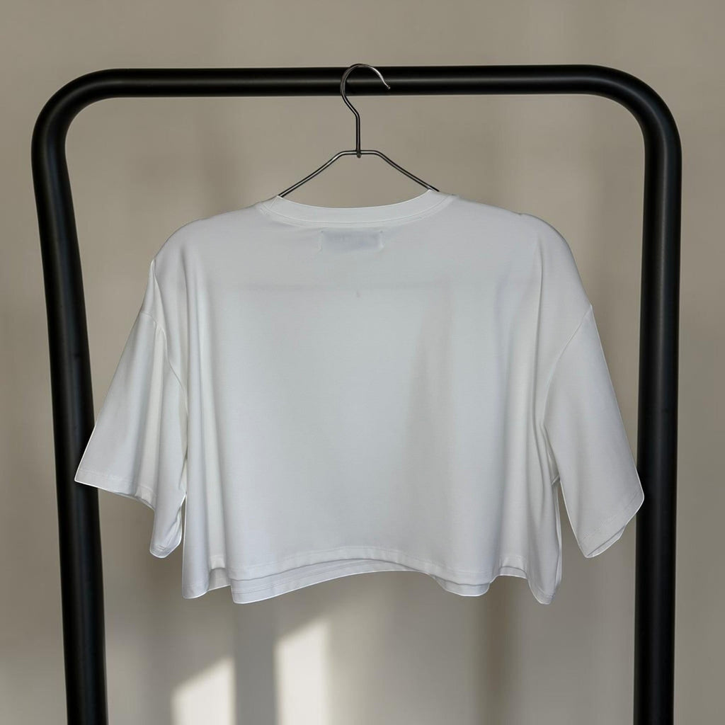 PBGC white Clubhouse crop top with a relaxed boxy fit and crew neckline hanging on a black rack