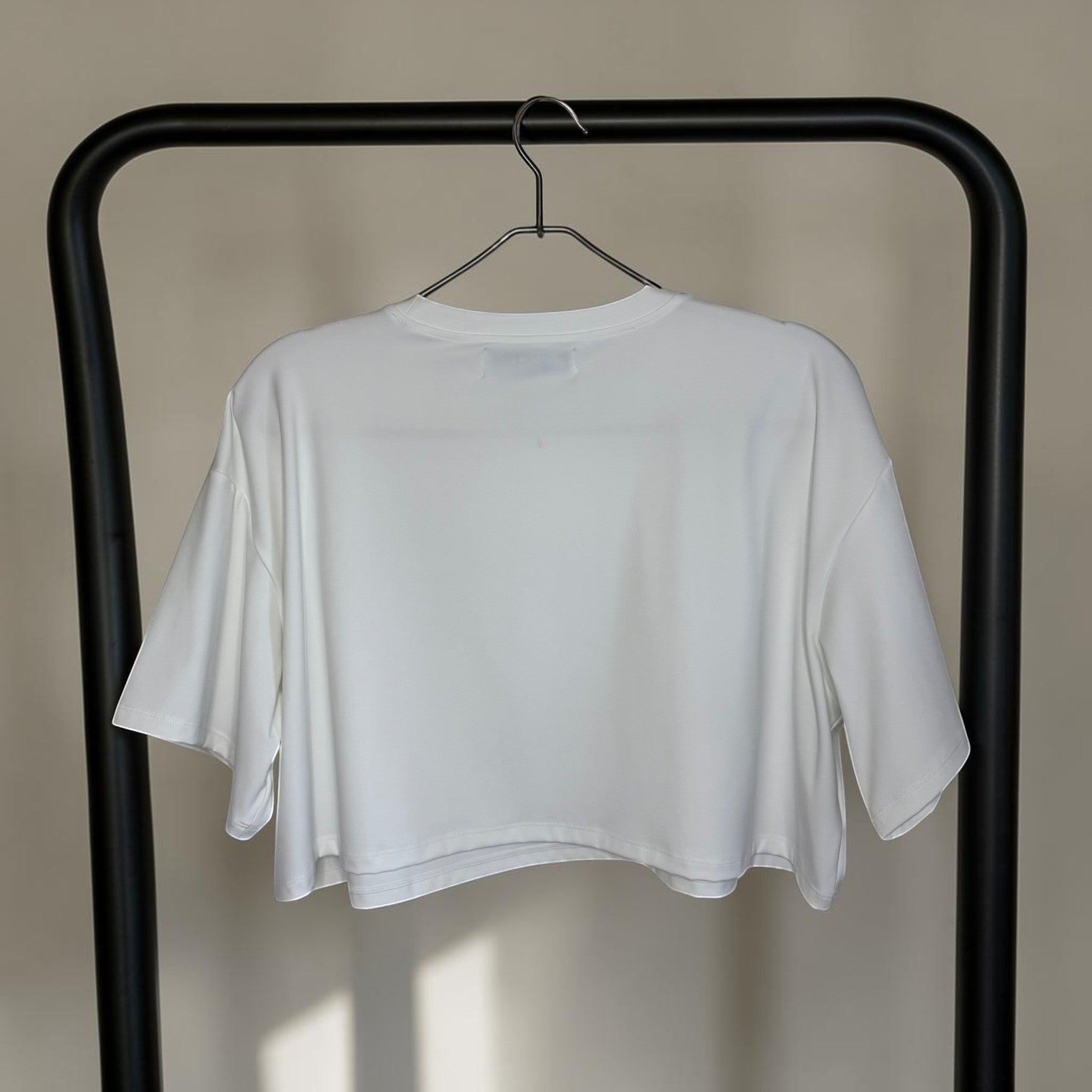PBGC white Clubhouse crop top with a relaxed boxy fit and crew neckline hanging on a black rack