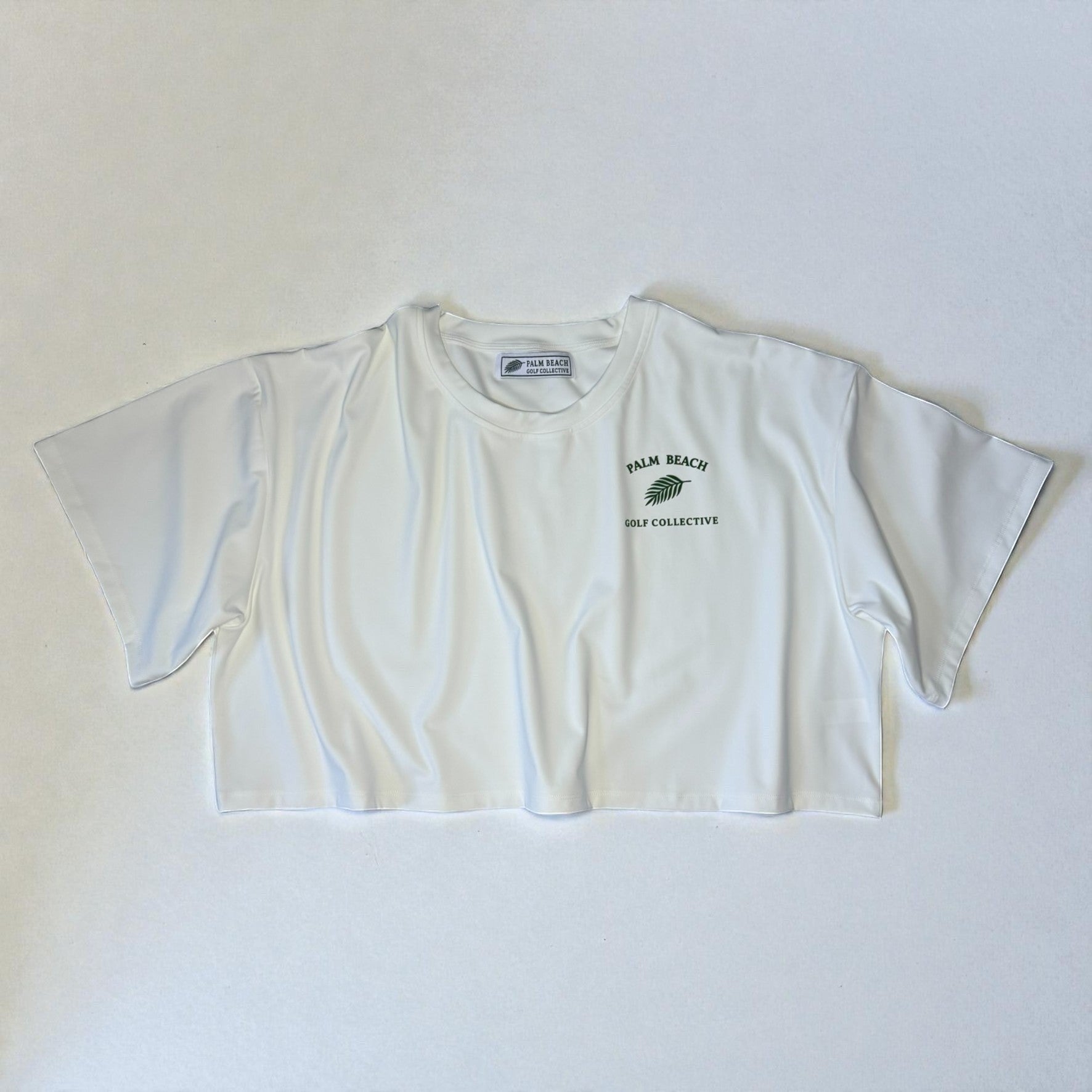 PBGC white crop top with a relaxed boxy fit, crew neckline, and green Palm Beach Golf Collective chest logo.