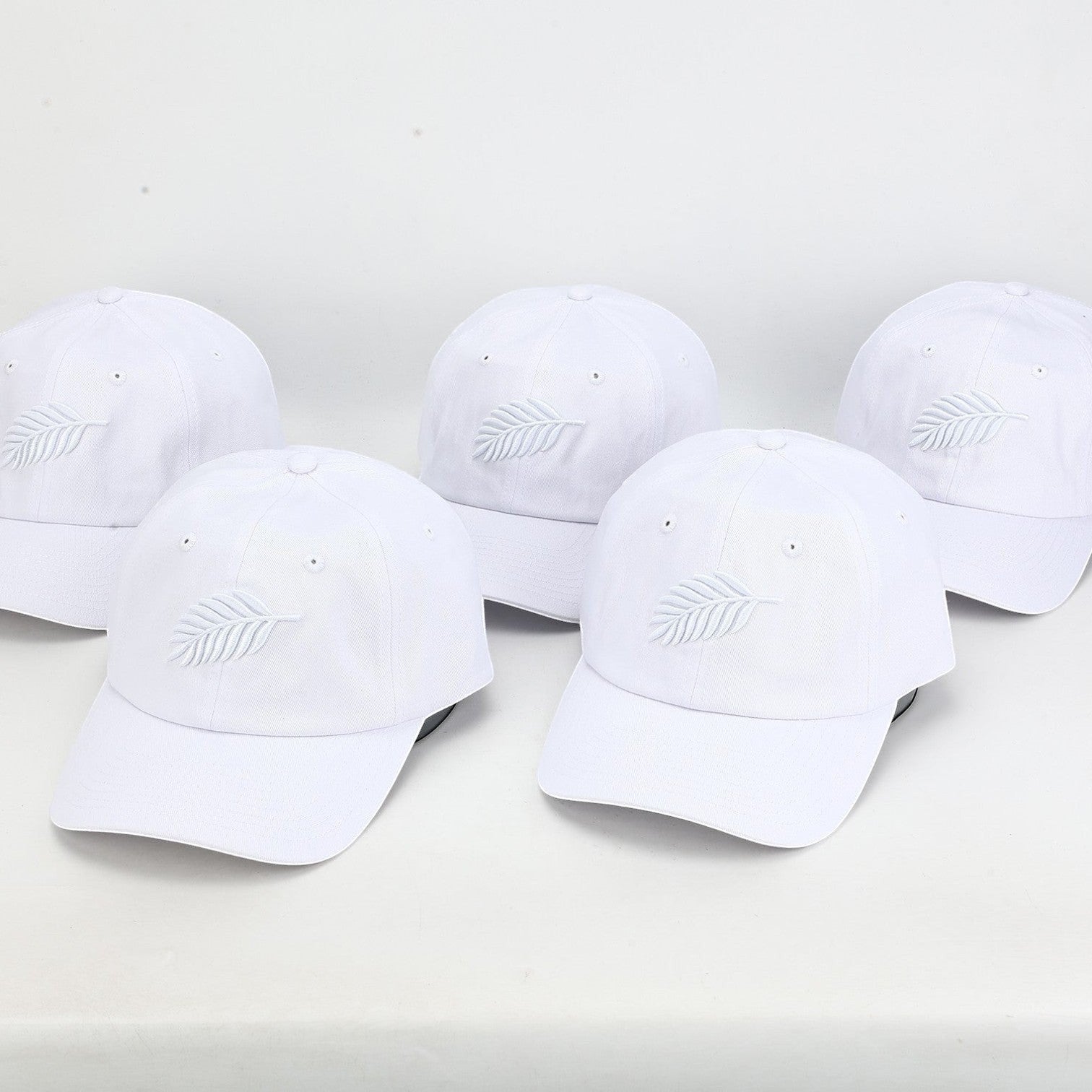 PBGC white cotton twill baseball caps with tonal embroidered fern leaf detail arranged in a group.