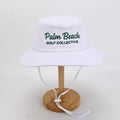 PBGC white bucket hat with green Palm Beach Golf Collective embroidery and adjustable chin strap for golf.