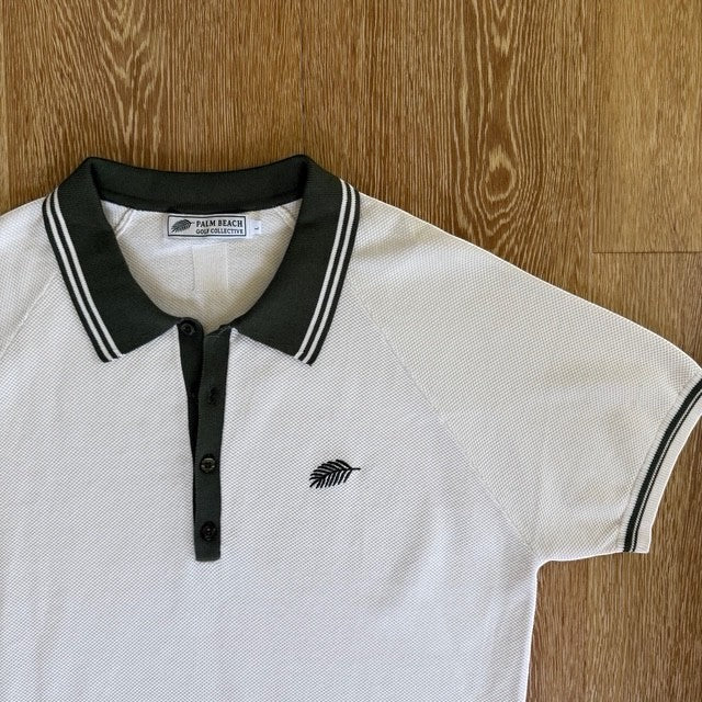 PBGC Course Record white knit polo shirt with olive green collar, button placket, and palm leaf logo embroidery.