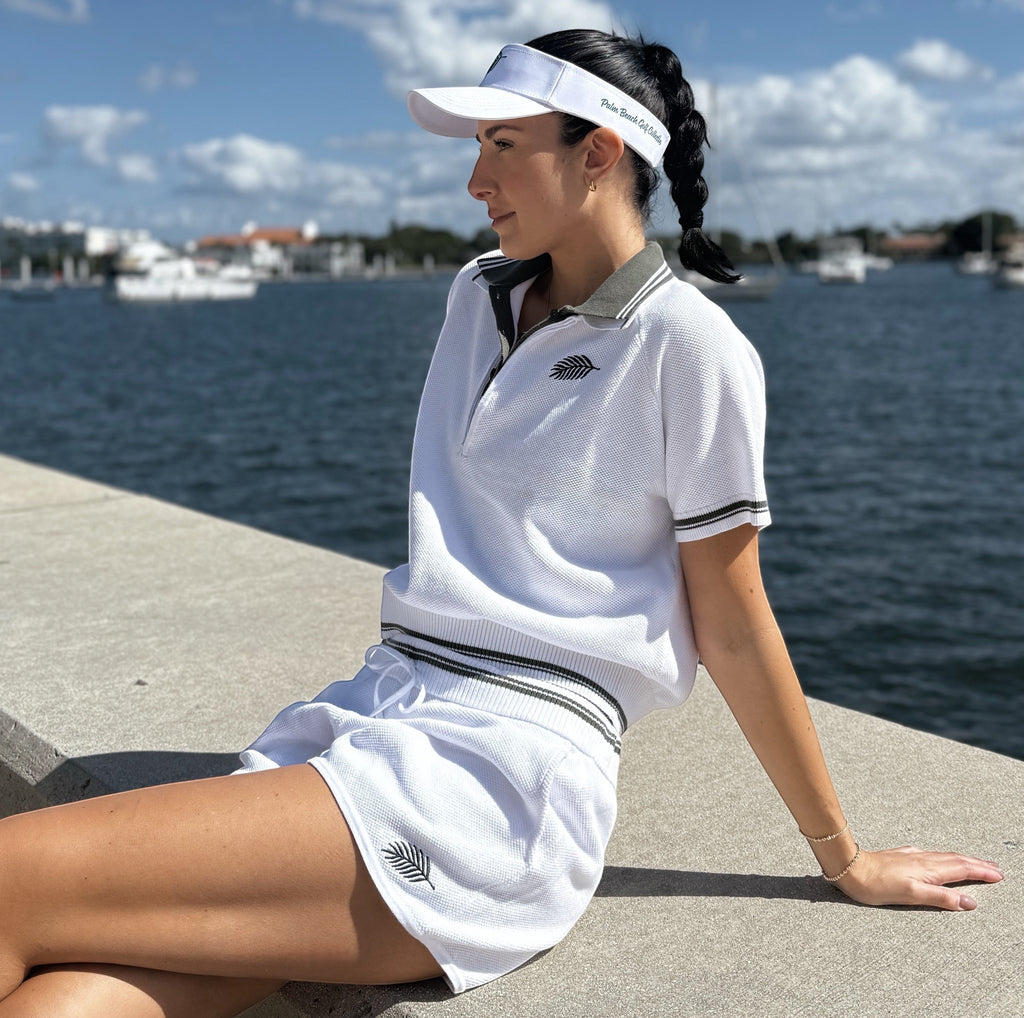 PBGC white short-sleeve knit quarter-zip sweater with dark green trim and palm logo worn by a woman outdoors