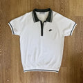 PBGC white knit golf polo with olive green collar, striped trim, and palm leaf embroidery on the chest.