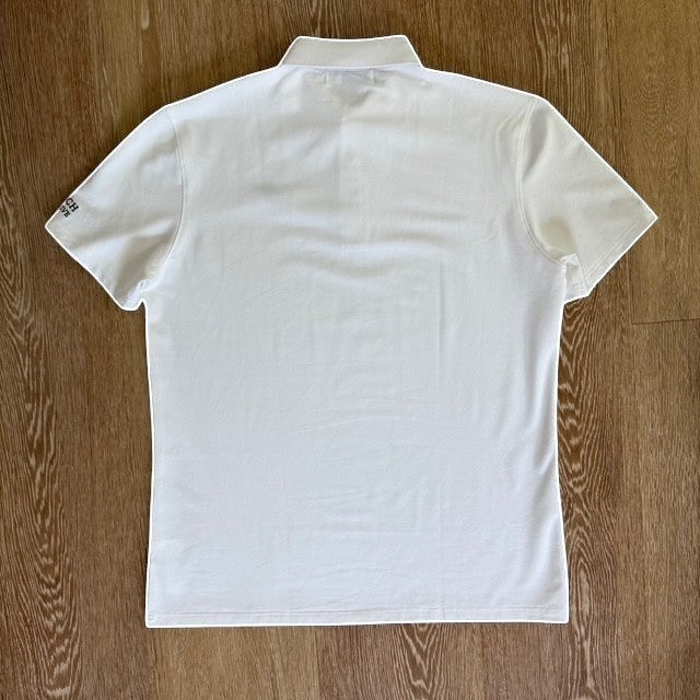 Back view of a PBGC white moisture-wicking performance golf polo shirt with short sleeves on a wooden background.