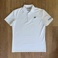 PBGC white performance golf polo with a palm leaf chest logo and sleeve branding on a wooden background