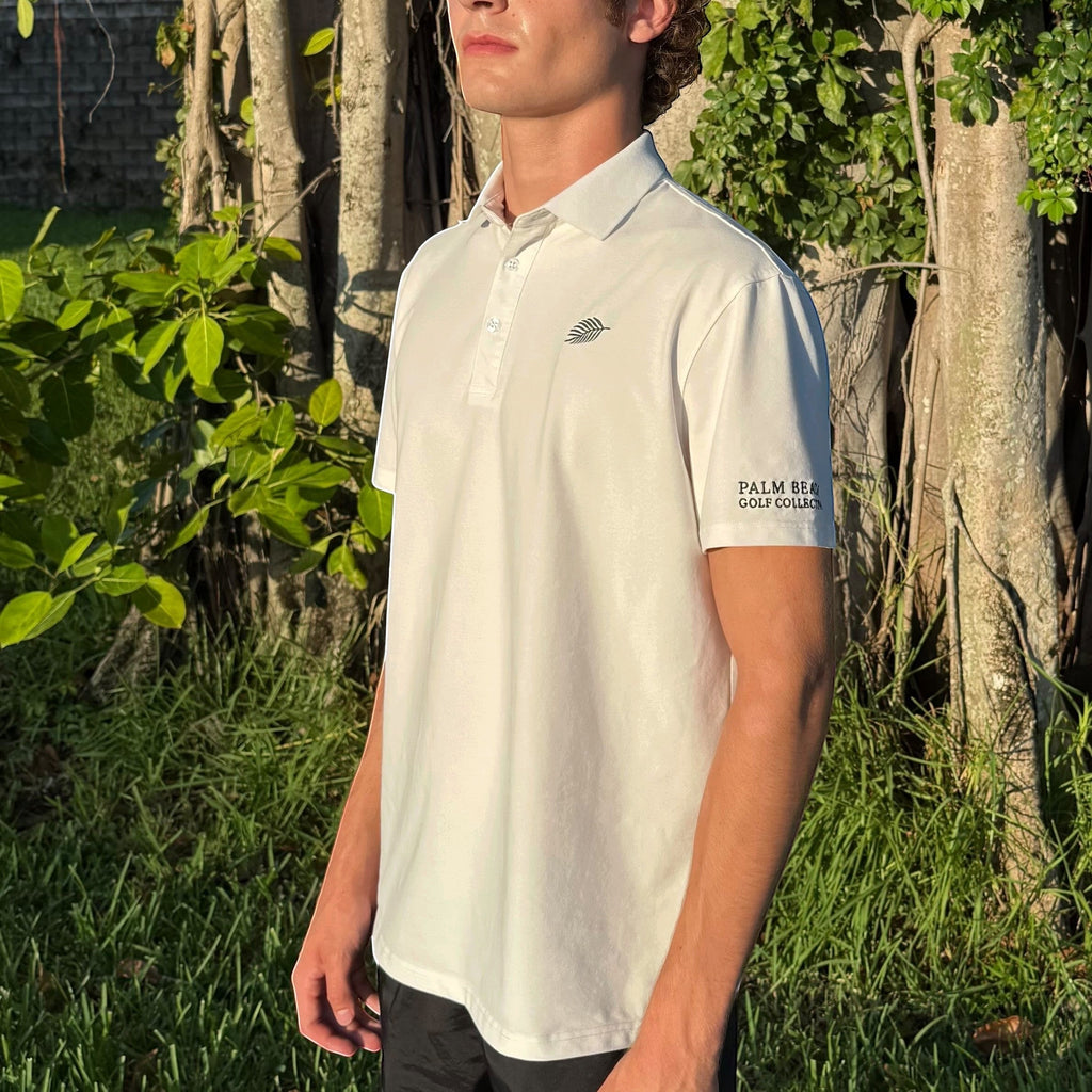 PBGC white performance golf polo with palm leaf logo and sleeve branding worn by a man in a sunny outdoor setting