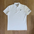 PBGC white performance golf polo with a green palm leaf chest logo and sleeve branding on a wooden background