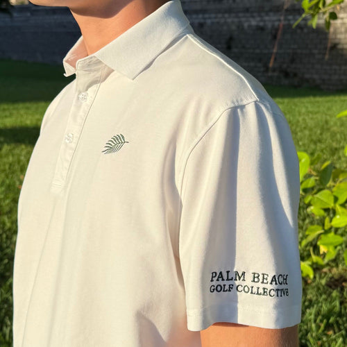 PBGC white performance golf polo with green palm leaf chest logo and sleeve branding worn outdoors