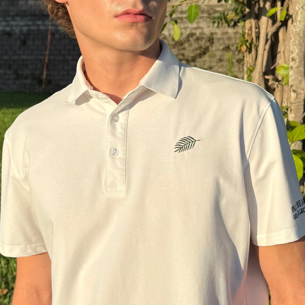 PBGC One Under Par white performance golf polo with palm leaf logo on chest and sleeve branding worn by a man