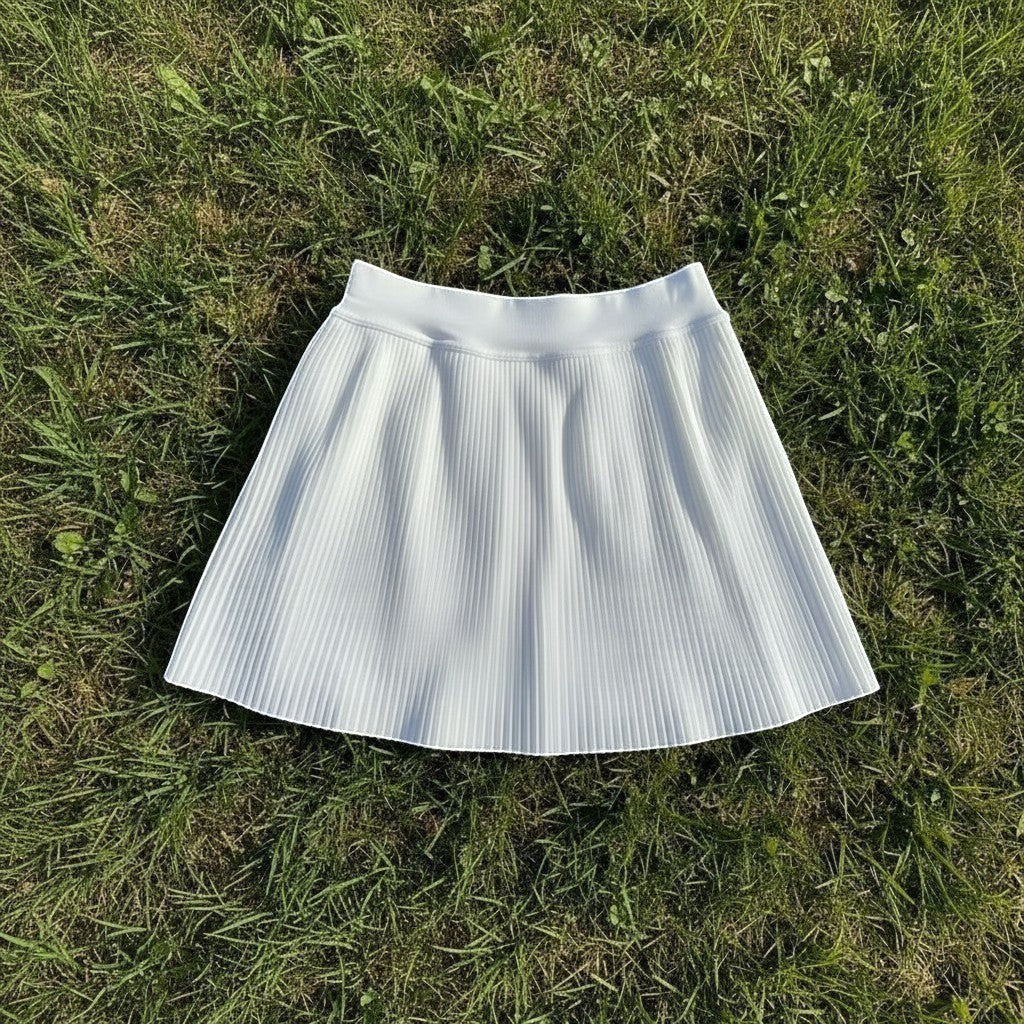PBGC white pleated athletic skort with built-in shorts, featuring a high-waisted design on a grassy background.