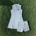 PBGC white sleeveless performance golf dress with mock neck, quarter-zip, and matching undershorts on green grass.